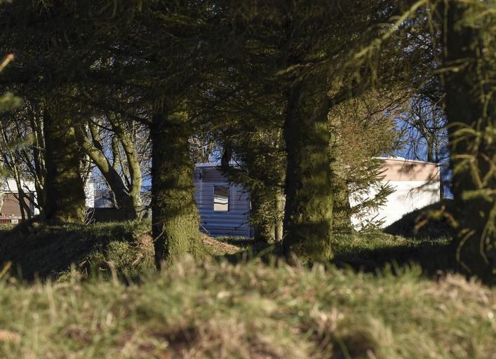 Mobilný dom zaparkovaný za vysokou trávou a stromami.jpg
